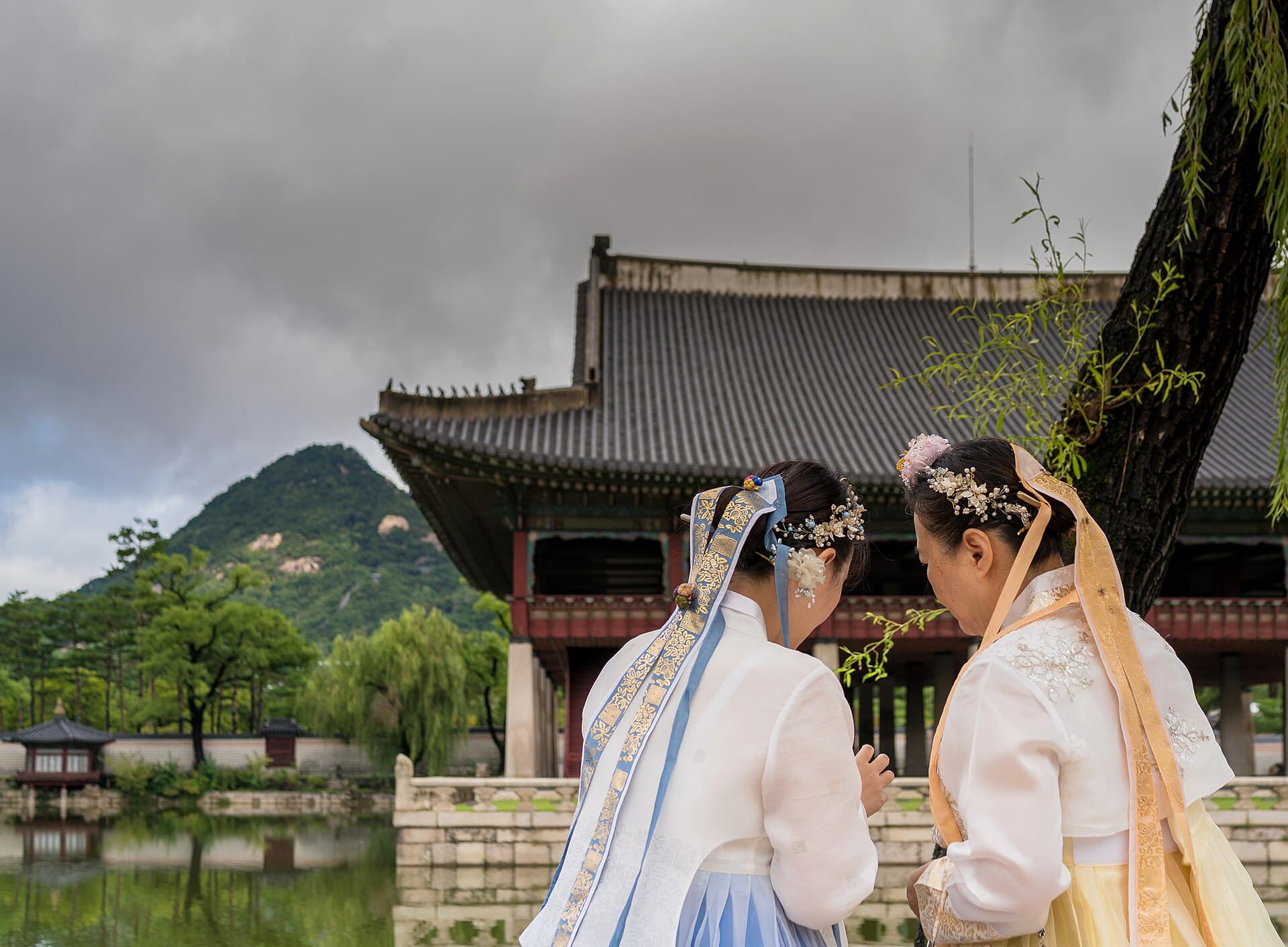 Visitors in hanbok beside a palace pavilion and pond in Seoul